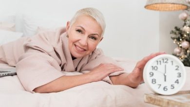 smiley-mature-woman-bathrobe-posing-bed-with-clock_23-2148419225-3058397