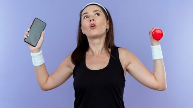 young-fitness-woman-headband-holding-smartphone-dumbbell-looking-confused-standing-blue-wall_141793-61159-2244002